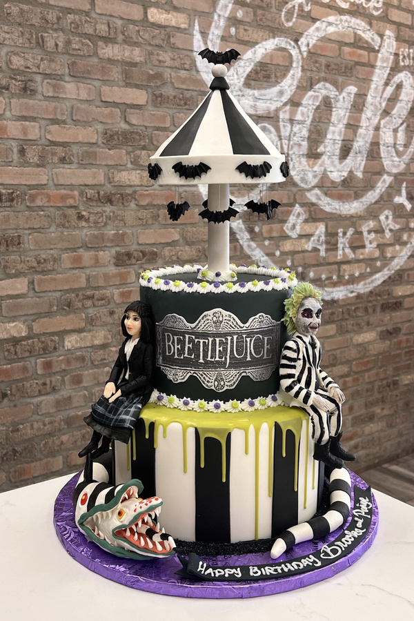 Beetlejuice-themed birthday cake with sculpted characters, sandworm, striped tiers, bats and carousel topper.
