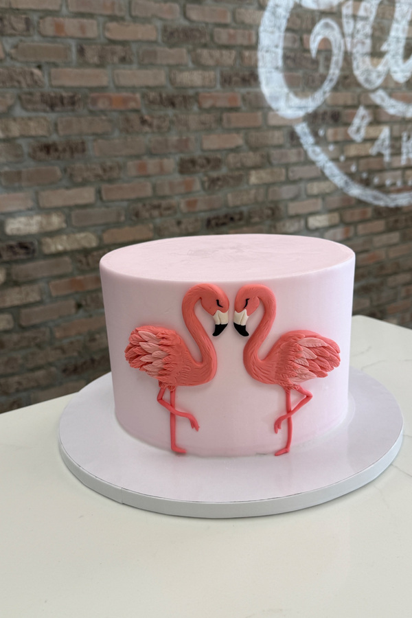 Cake decorated with two handcrafted flamingos facing each other in a heart-shaped pose.