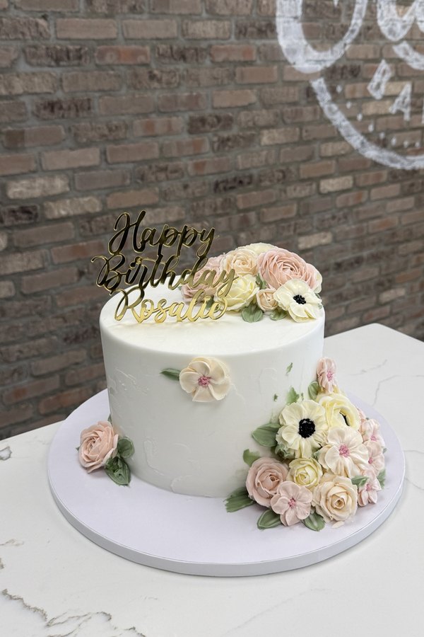 Buttercream birthday cake with handcrafted flowers, roses, leaves and Happy Birthday topper.