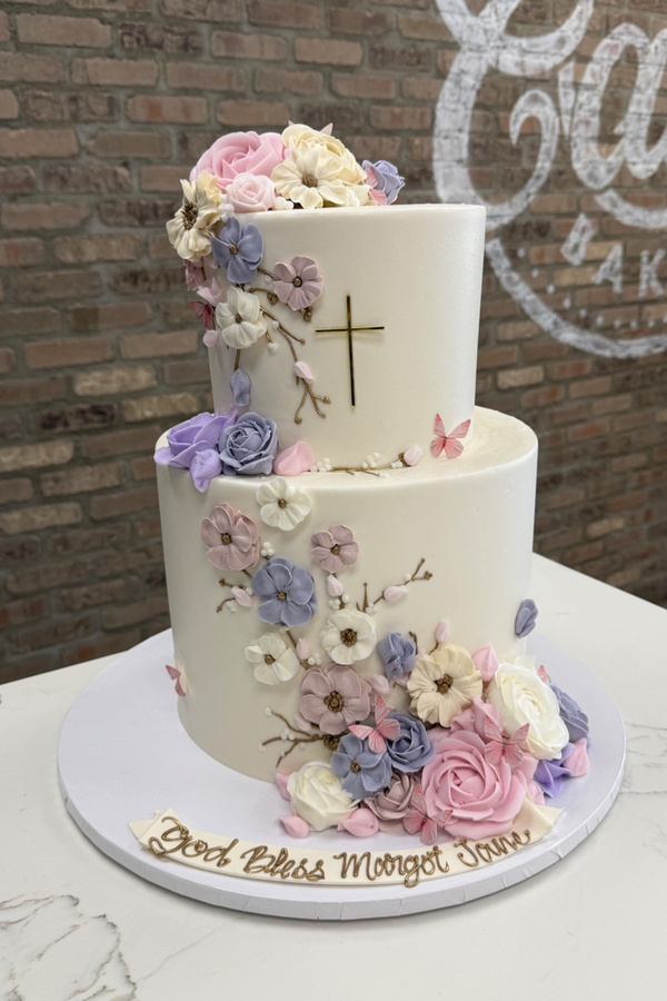 Two-tier religious cake with cross, fancy buttercream flowers, roses, branches and butterflies.
