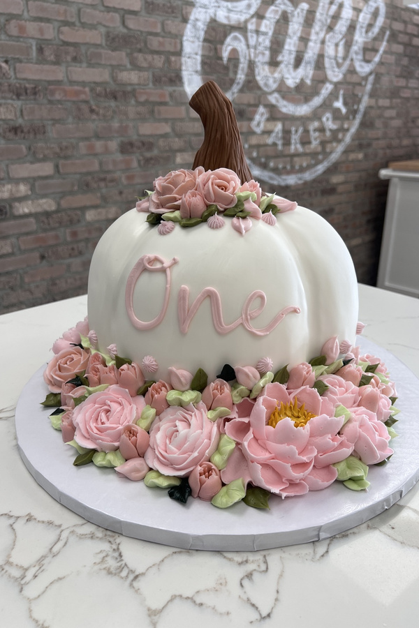 Pumpkin-shaped first birthday cake with fancy buttercream flowers, roses, leaves and One inscription.
