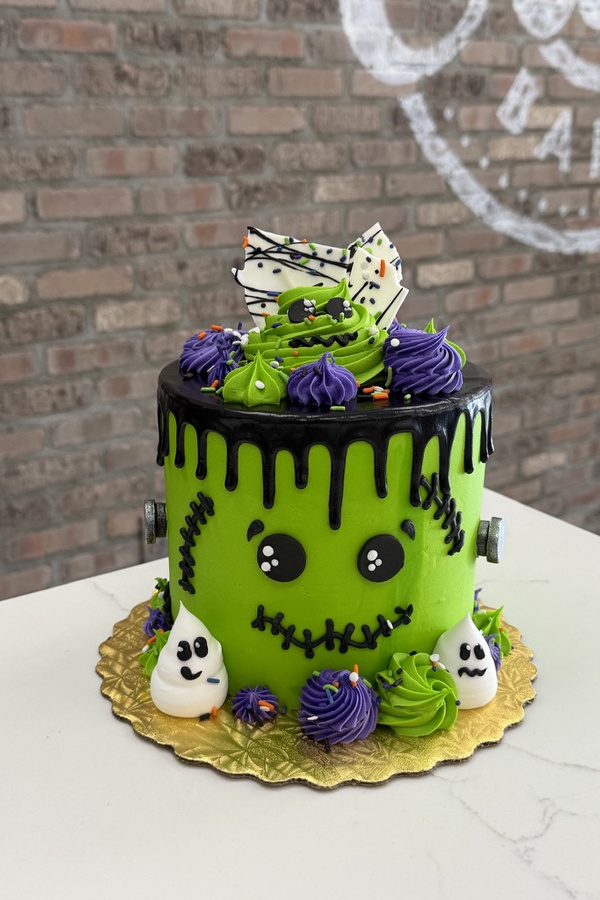Frankenstein Halloween cake with monster face, stitched details, bolts, black drips, buttercream swirls and ghosts.