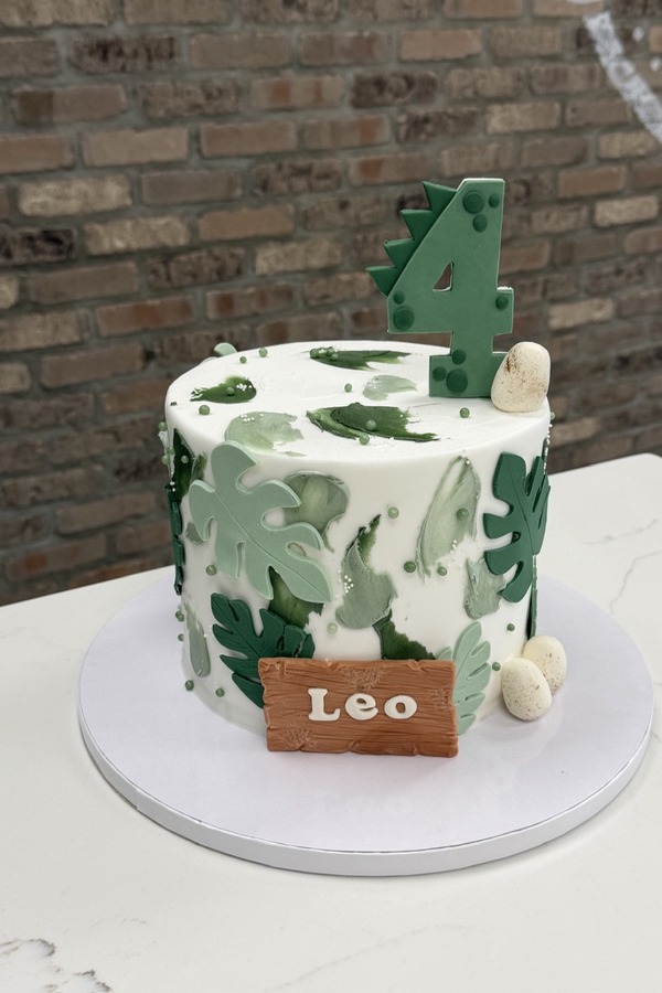 Dinosaur 4th birthday cake with green tropical leaves, dinosaur eggs, number 4 and personalized name plaque.