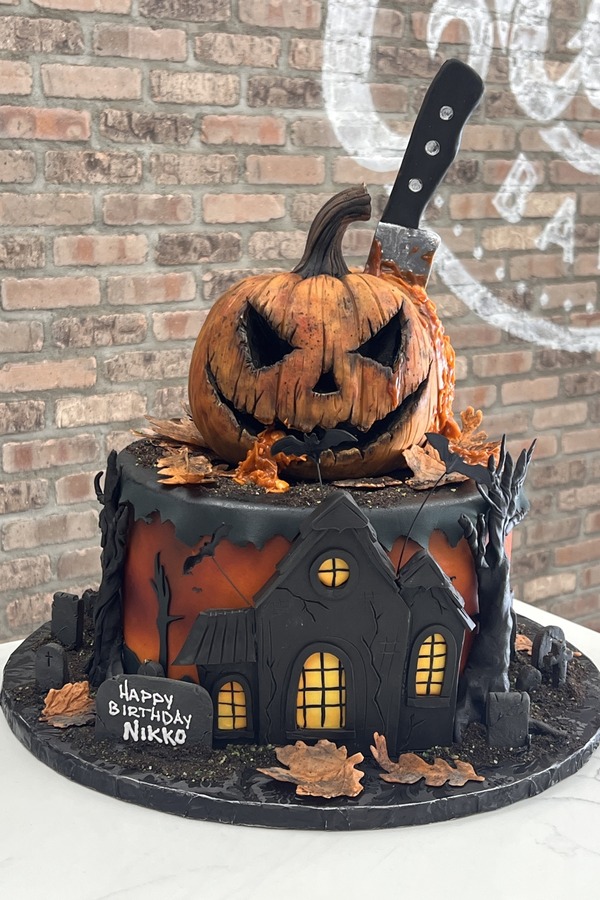 Halloween cake with sculpted jack-o’-lantern, haunted house, knife, gravestones, bats and twisted trees.