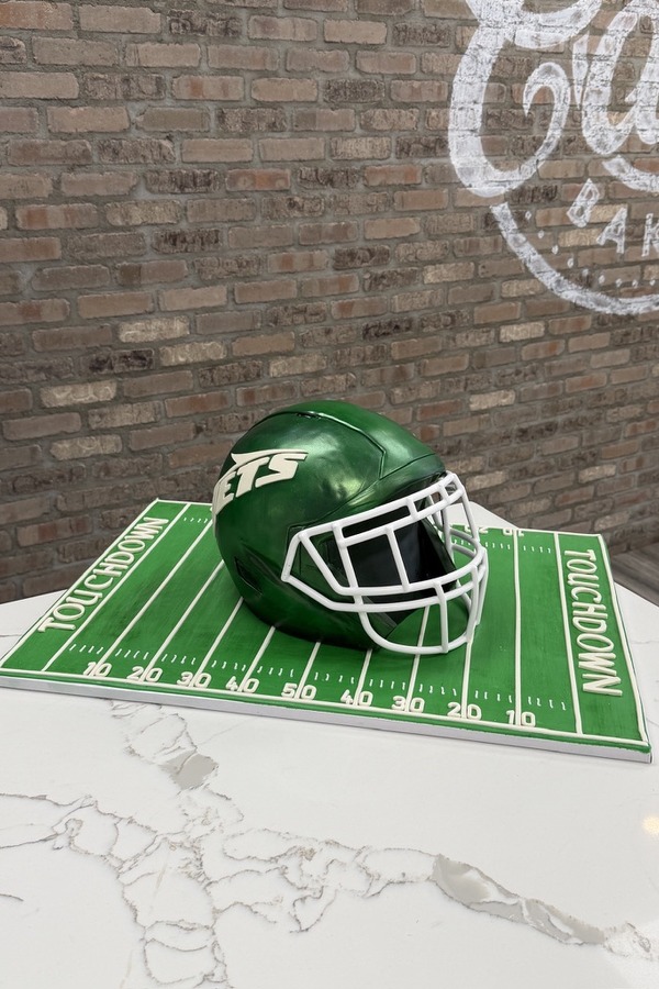 New York Jets football helmet cake with green football field and white goal line details.