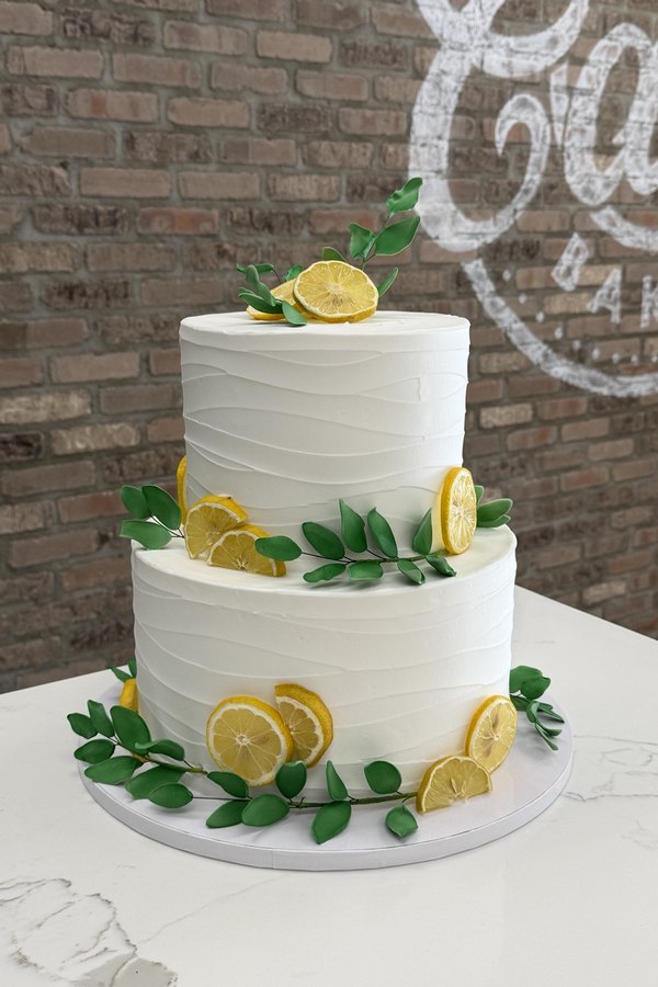 Two-tier buttercream cake decorated with lemon slices, greenery and leafy branches.