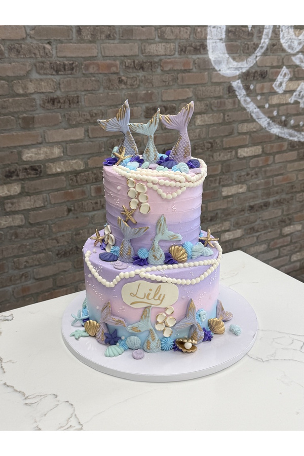Two-tier mermaid birthday cake with sculpted mermaid tails, seashells, starfish and pearl decorations.