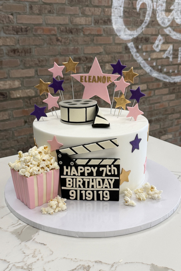 Movie birthday cake with film reel, clapperboard, popcorn and personalized star toppers.