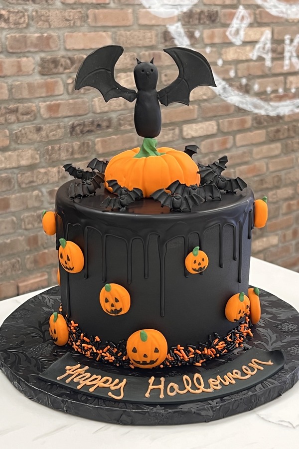 Halloween cake with jack-o’-lanterns, sculpted bats, pumpkin centerpiece and drip detail.