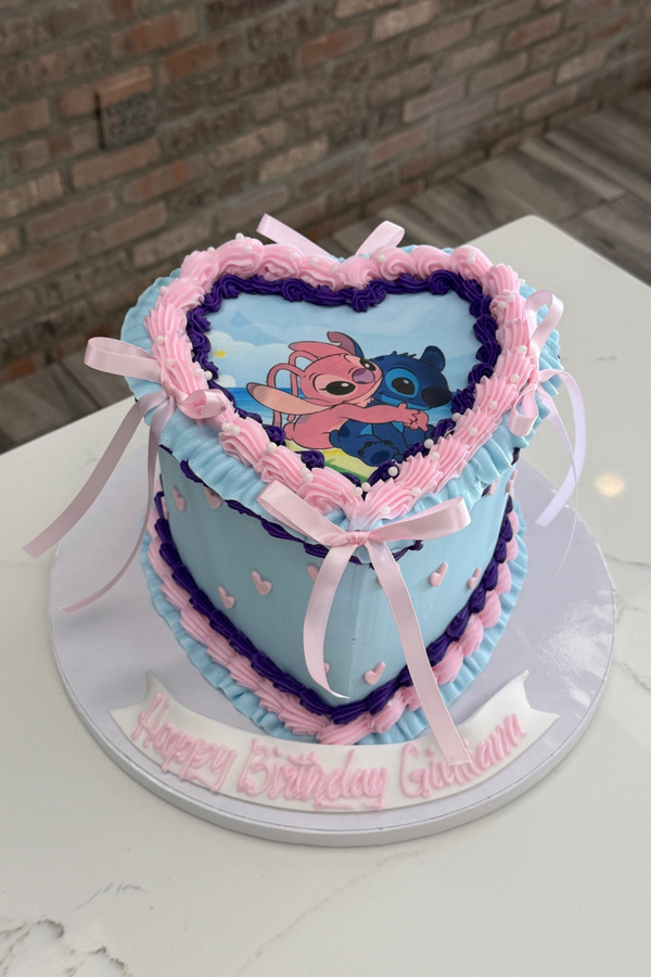 Heart-shaped Stitch and Angel birthday cake with piped buttercream borders, pearls and ribbon bows.