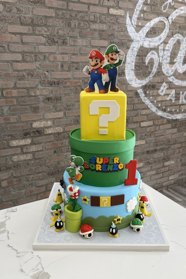 Three-tier Super Mario first birthday cake with Mario, Luigi, Yoshi, question block, pipes, mushrooms and stars.